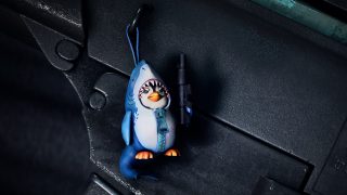 Uma estatueta de um pinguim segurando um fuzil em um traje de tubarão.