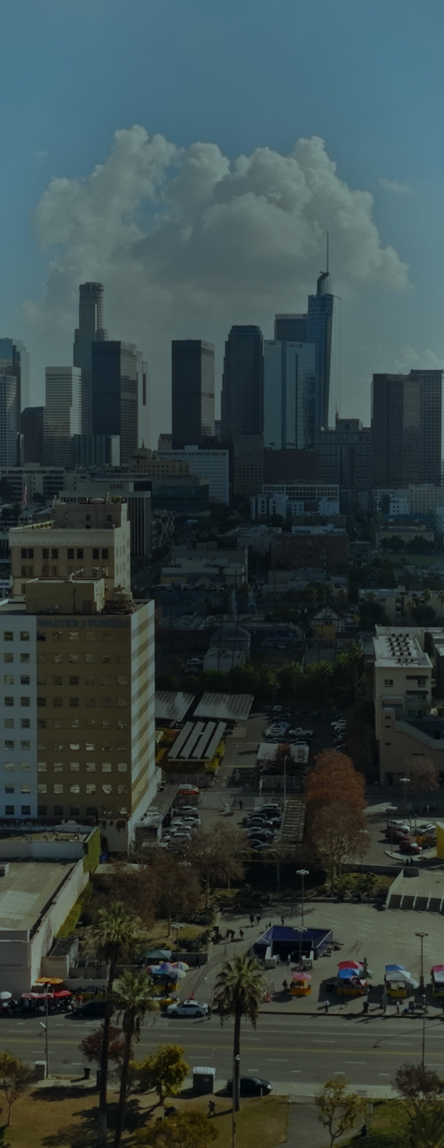 An urban city scape with buildings of varying heights against a blue sky and clouds. 