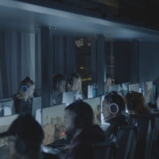 Two rows of people wearing headsets seated in front of computer screens playing a first person shooter