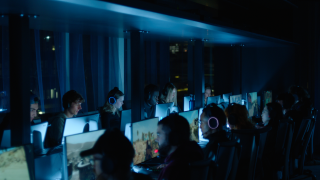 Gamers focused on screens in a dimly lit room, wearing headphones, immersed in gameplay.