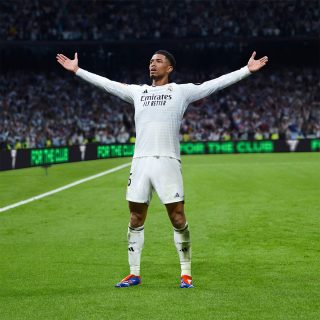 Jude Bellingham em uma pose vitoriosa em um campo de futebol.