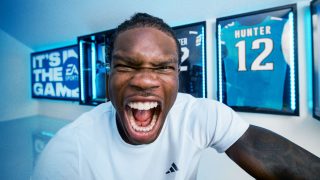 A close up of Travis Hunter yelling energetically, while behind him are his jerseys and EA Sports branded promotions.