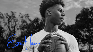 Picture of Elijah Haven in black and white holding a football, looking away from the camera. His signature in blue is in the left bottom corner. 