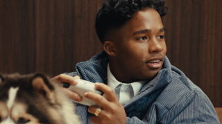 Picture of Endrick holding a game controller, sitting behind his dog. He is looking to the side.