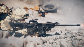 A soldier lies in a prone position on rocky terrain whilst holding a large gun and looking down a scope.
