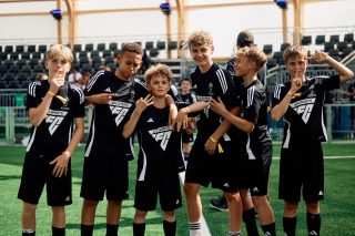 A group of young players in EA SPORTS FC jerseys celebrate together on a football pitch, representing the positive impact of the EA SPORTS FC FUTURES program.