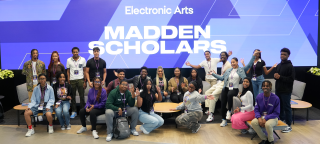 A group of Black men and women gather in front of an electronic sign to take a group photo. The sign contains the text “Electronic Arts – MADDEN SCHOLARS.