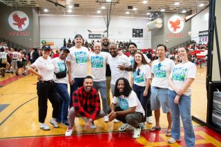 A group of Black men and women gather in front of an electronic sign to take a group photo. The sign contains the text “Electronic Arts – MADDEN SCHOLARS.