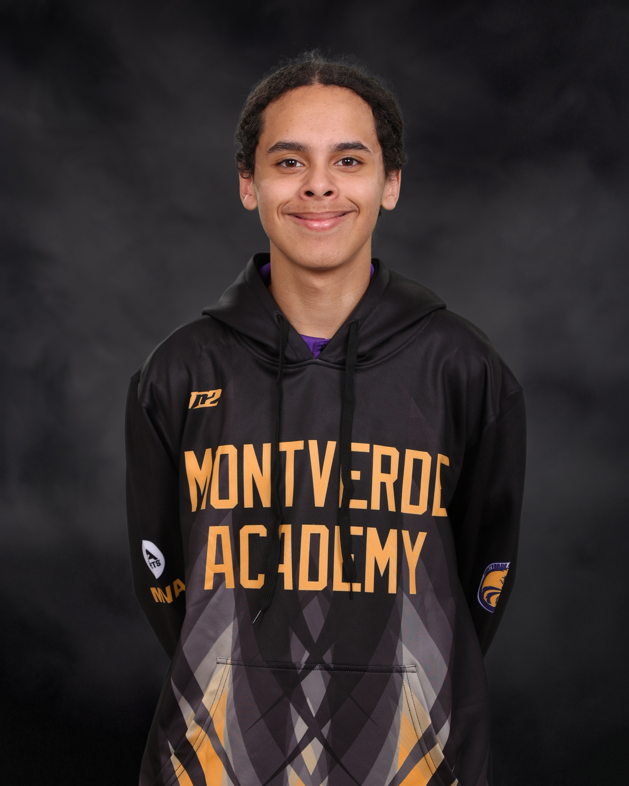 A young male student with black hair smiles at the camera for a photo against a black background. The student is wearing a sweatshirt that reads “MONTVERDE ACADEMY.”