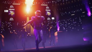 A football player in a purple uniform runs onto a field with a flaming entrance and purple lights. The crowd holds up glowing devices, creating a starry backdrop.
